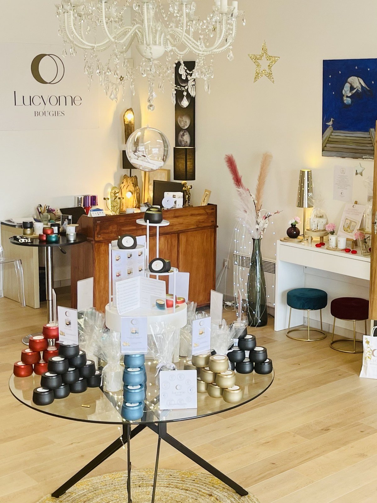 La table de verre des Lucyometes : les boites metal noires, rouges, bleues et dorees empilees avec leurs cartes, sous le lustre de cristal et l'enseigne Lucyome Bougies.